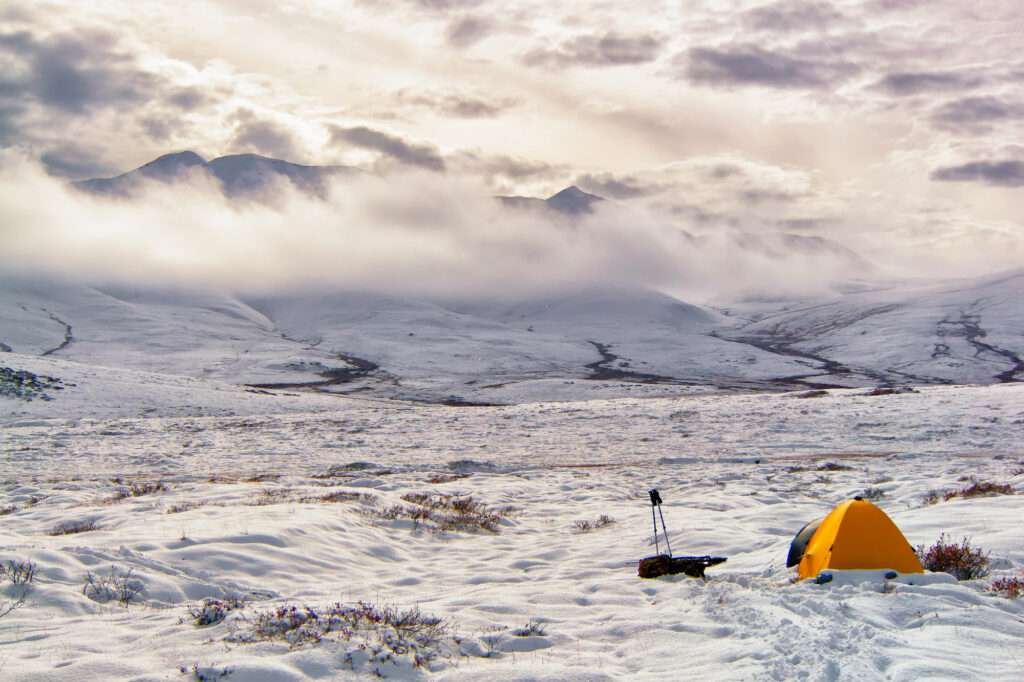 A tent and backpack rest on the freshly snow-covered tundra in Alaska hunting in the Arctic North Slope
