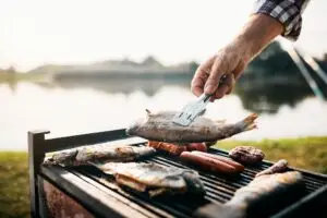 Close-up of man grilling fish on barbecue grill while camping by the river.