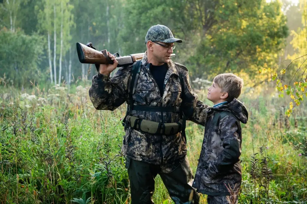 Father with gun showing something to son while hunting on a nature
